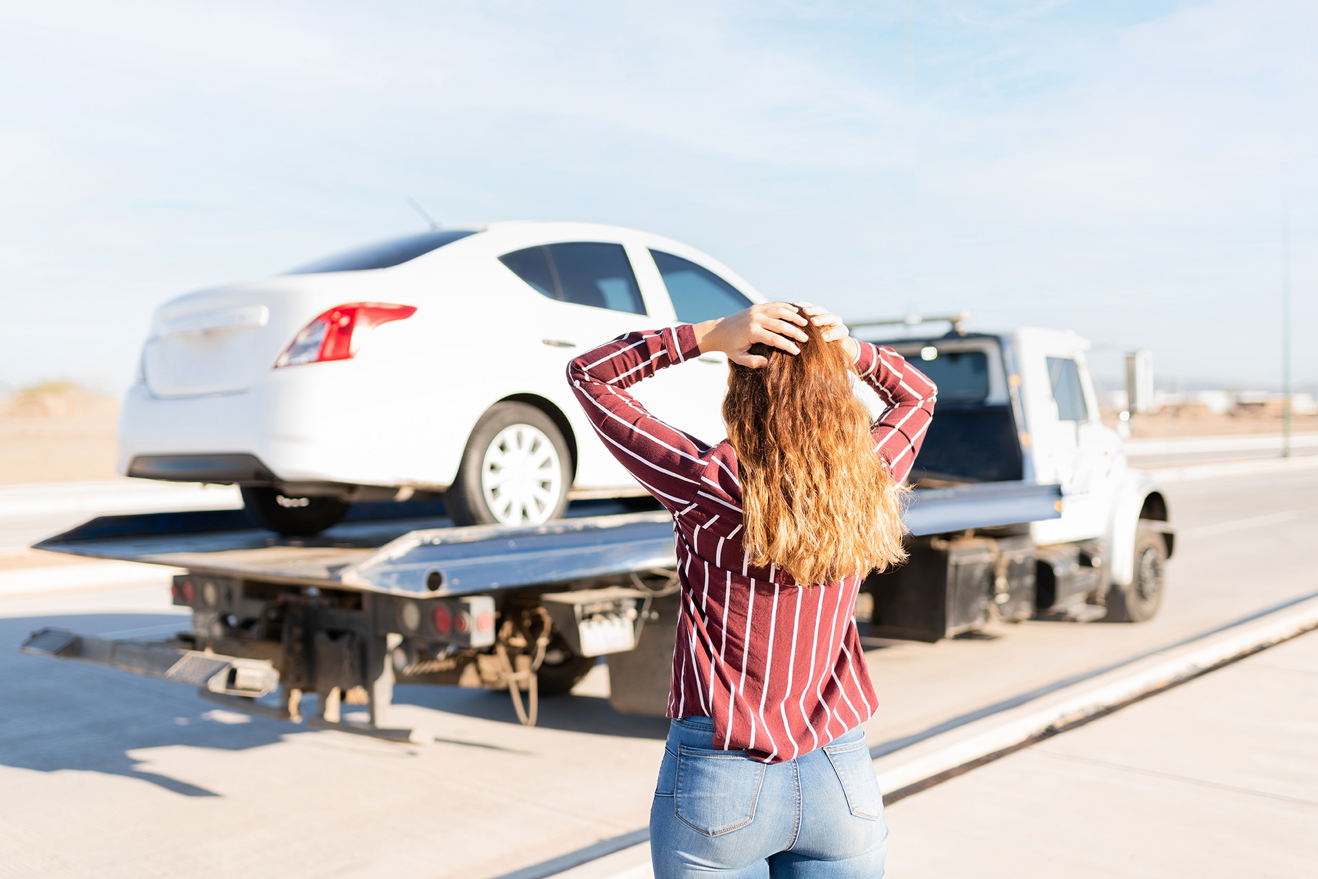 Rear view of an angry woman watching her car on a tow truck