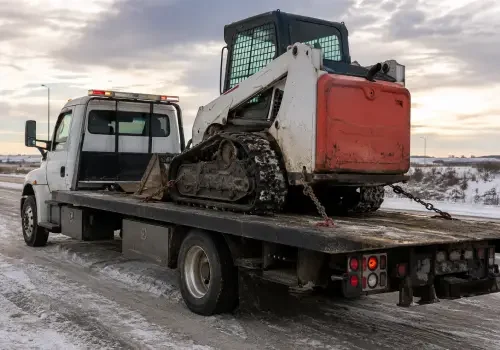 Flatbed tow truck hauling construction equipment in Calgary